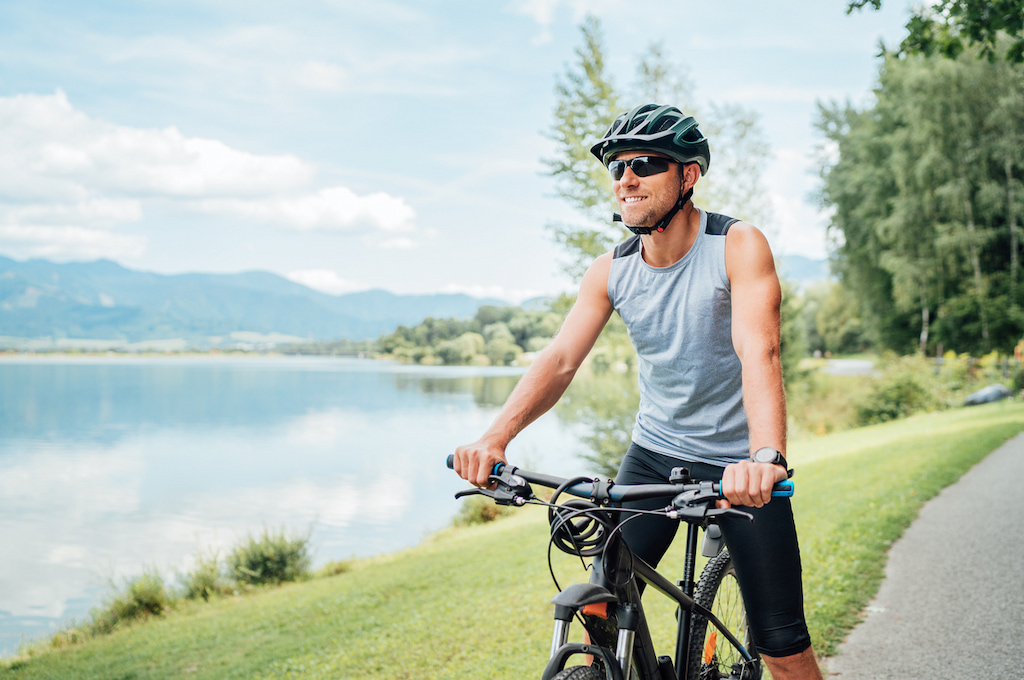 Mann auf Rad, im Hintergrund ein See. Radfahren ist im Norden Salzburgs mit Radwegen um die Trumer Seen besonders idyllisch. 